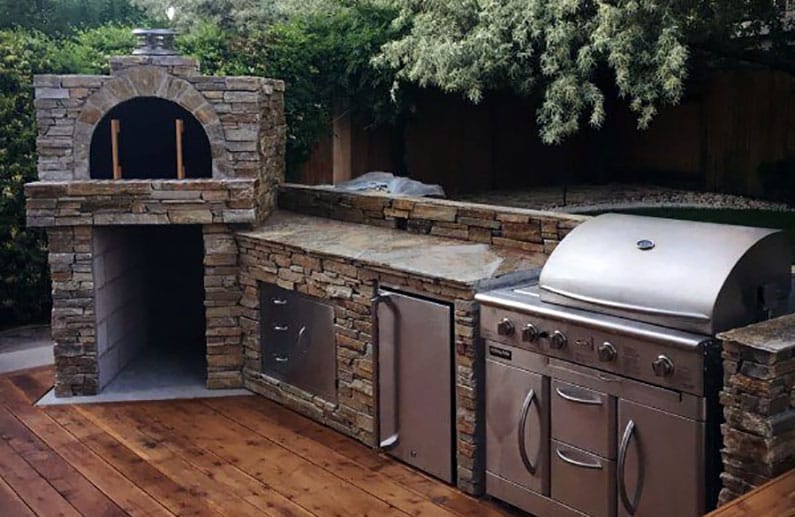 A beautifully organized outdoor kitchen featuring a wood-fired pizza oven and grilling station.